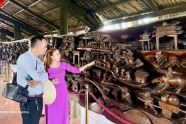 Los visitantes admiran una gigantesca obra de arte en madera fósil, de casi 25 metros de longitud y unas 20 toneladas de peso, considerada una de las piezas más elaboradas de Vietnam. (Foto: VNA)