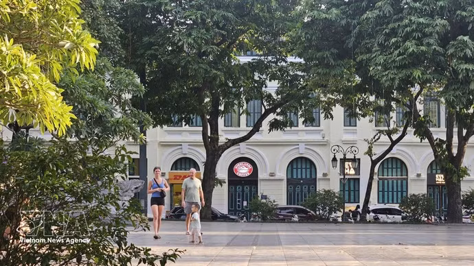 Turistas extranjeros pasean bajo los árboles frondosos a orillas del lago Hoan Kiem, disfrutando del ambiente fresco de la capital. (Foto: VNA)
