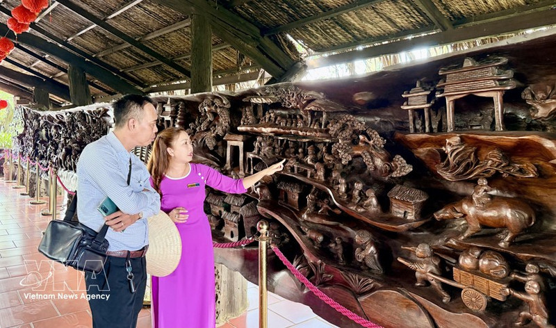 Los visitantes admiran una gigantesca obra de arte en madera fósil, de casi 25 metros de longitud y unas 20 toneladas de peso, considerada una de las piezas más elaboradas de Vietnam. (Foto: VNA)