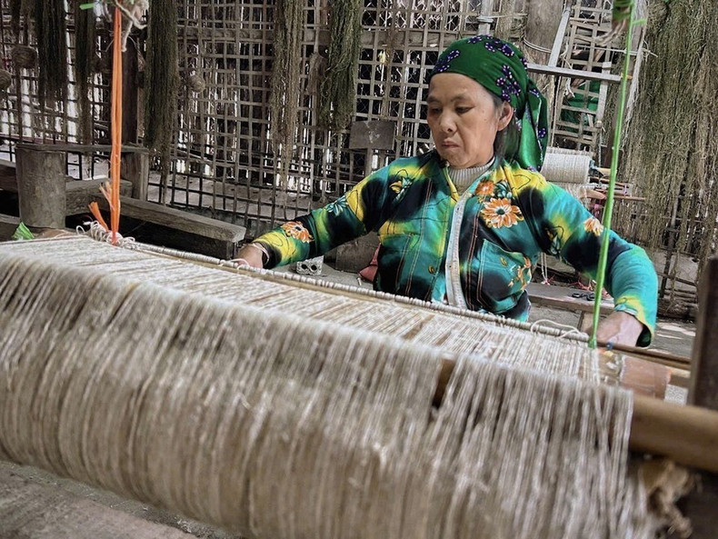 Una mujer Hmong en la aldea textil Lung Tam tejiendo telas a mano en telares de madera tradicionales.