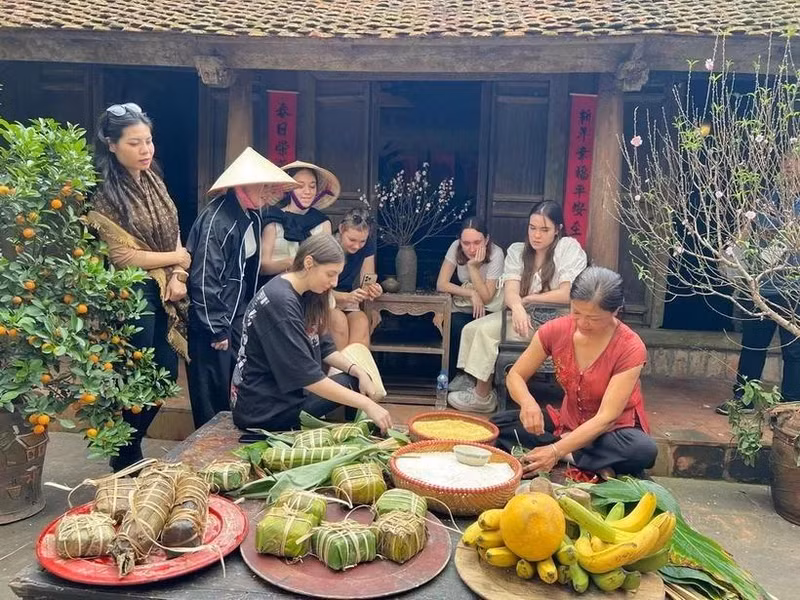 Los visitantes internacionales experimentan la envoltura de Banh Chung en la antigua aldea de Duong Lam. (Foto: VNA)