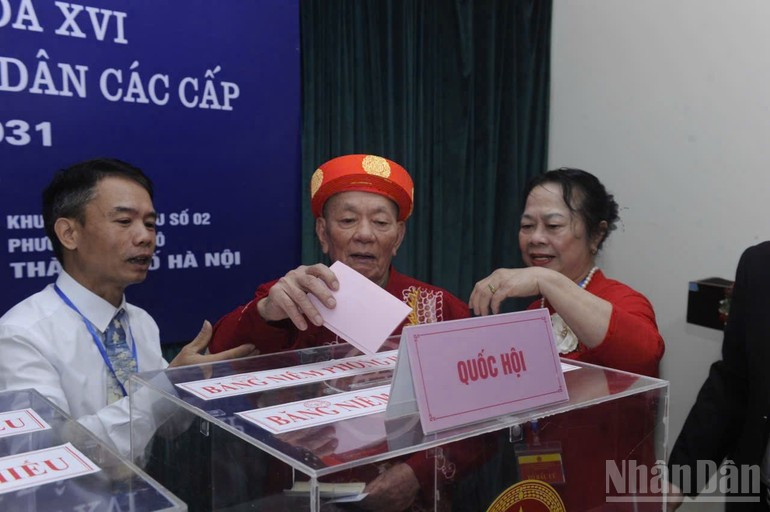 Un anciano ataviado con la túnica tradicional “ao dai” entra en la sala de votación con la ayuda de funcionarios. La escena, tomada en la circunscripción electoral 2 en el barrio de Nghia Do, en Hanói, emociona a quienes están alrededor.