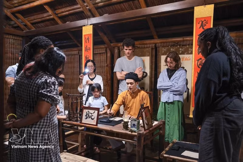 Los visitantes observan a un calígrafo realizar una demostración de caligrafía en un espacio de cultura tradicional durante el recorrido nocturno por el Templo de la Literatura en Hanói. (Foto: VNA)