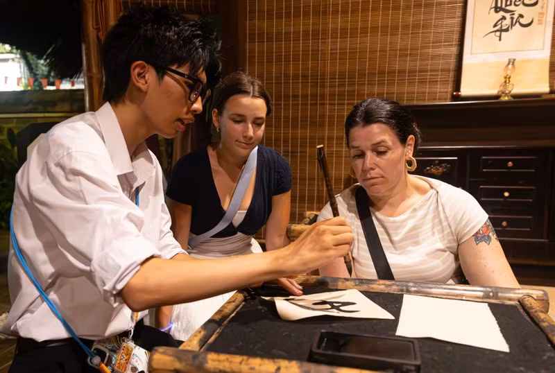 Turistas internacionales disfrutan de la experiencia del arte de la caligrafía con pincel bajo la guía de un promotor cultural. (Foto: VNA)