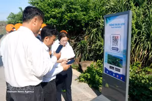 Un turista escanea un código QR para acceder rápidamente a la información turística en el mástil de la bandera de soberanía de la zona especial de Phu Quy (Lam Dong). (Foto: VNA)