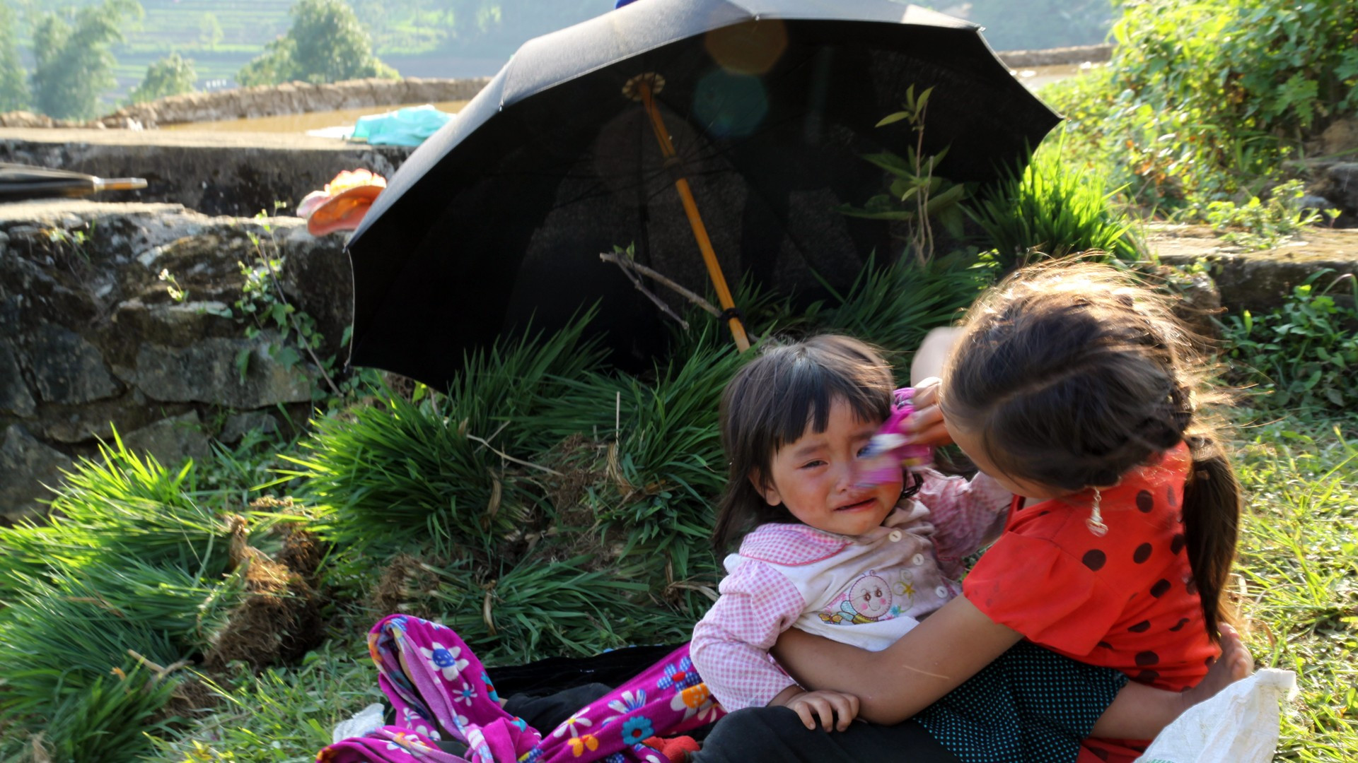 La niña cuida de su hermana para que los padres puedan labrar la tierra sin preocuparse.