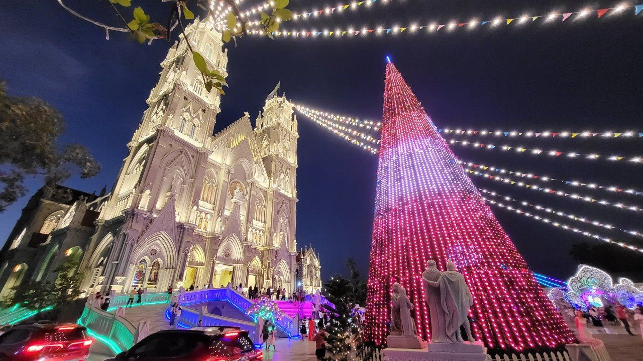El árbol de Navidad instalado frente a la iglesia animado con muchas luces.