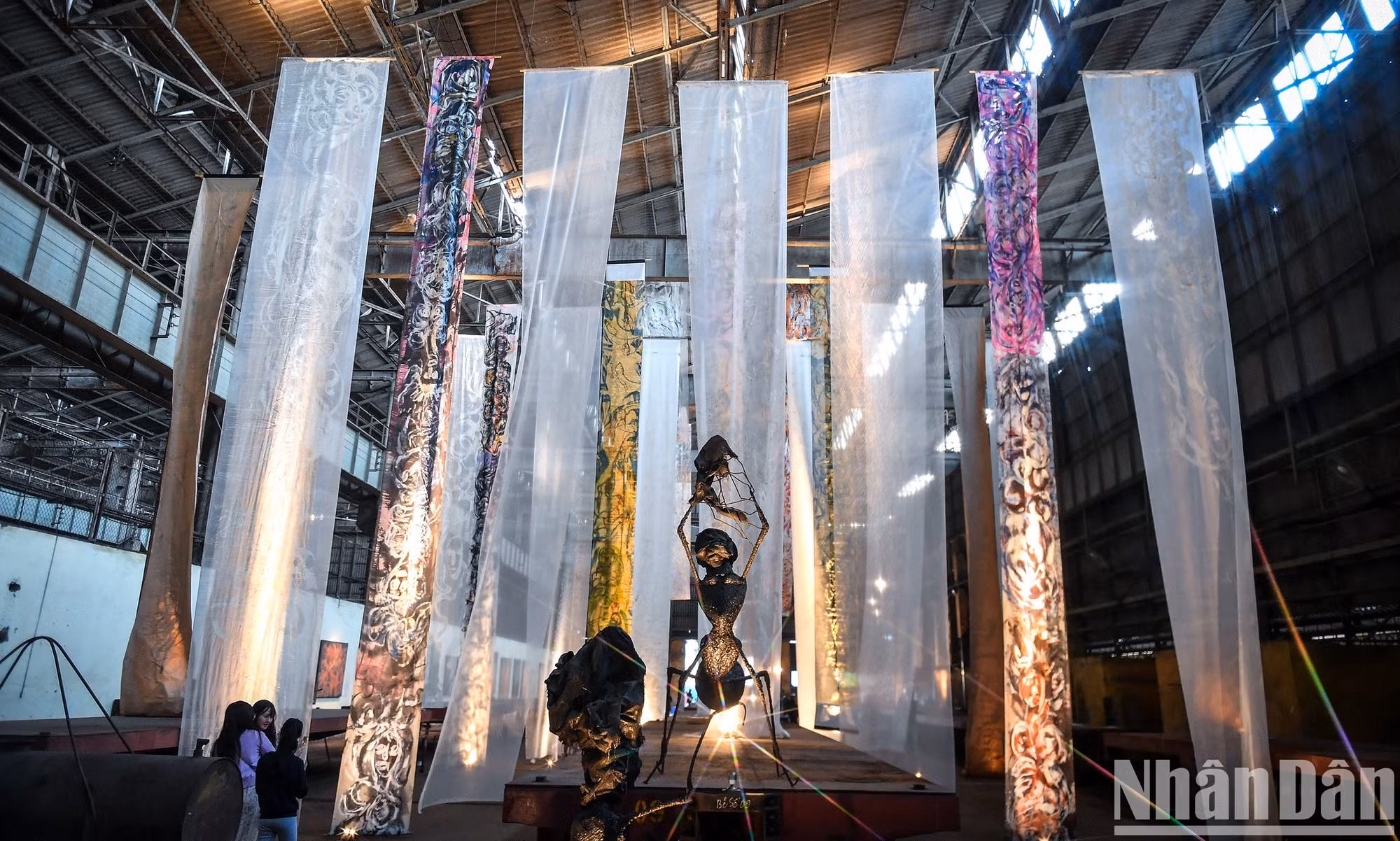 Instalación "El llamado", del artista Thu Tran, con tiras de pinturas de 40 a 60 metros de largo colgadas en el techo del taller 3B1. El colosal espacio mantiene el flujo del patrimonio cultural, así como el entrelazamiento entre lo viejo y lo nuevo, la memoria y el futuro.