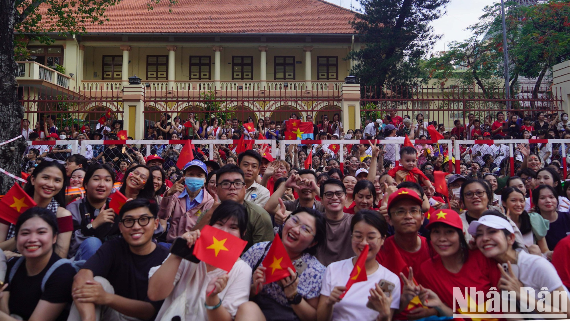 Los niños, con rostros radiantes, seguían a sus padres mientras esperaban el momento del desfile, sosteniendo banderas rojas con estrellas amarillas en sus manos.
