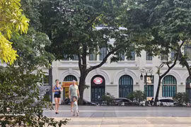 Turistas extranjeros pasean bajo los árboles frondosos a orillas del lago Hoan Kiem, disfrutando del ambiente fresco de la capital. (Foto: VNA)