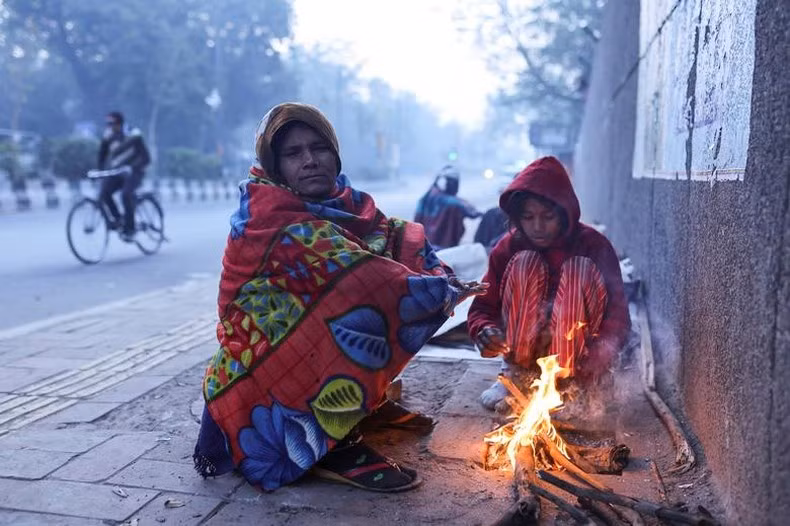Madre e hija encienden fuego en la acera en una fría mañana invernal en Nueva Delhi, India. La gente en la capital india ha sufrido un fuerte frío por estos días.