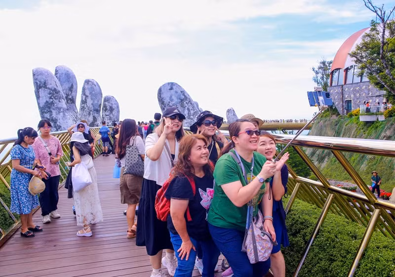 Turistas internacionales pasean con entusiasmo por el Puente Dorado, en el área turística Sun World Ba Na Hills.