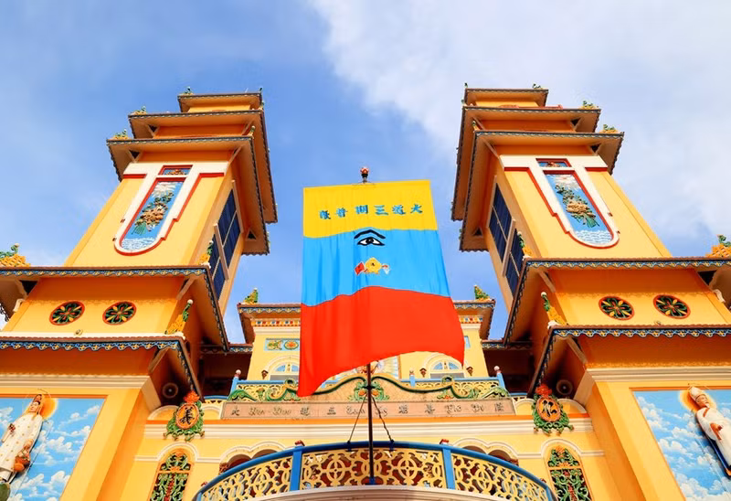 La bandera Cao Dai tiene tres colores: la parte amarilla está bordada con seis palabras en caracteres chinos que identifican el nombre completo de la orden Cao Dai. La parte azul está bordada con el Ojo Divino y los tres dharmas antiguos. La parte inferior es roja y representa el confucianismo mientras que los colores anteriores, amarillo y azul, corresponden al budismo y al taoísmo, respectivamente. (Foto: VNA) La bandera Cao Dai tiene tres colores: la parte amarilla está bordada con seis palabras en caracteres chinos que identifican el nombre completo de la orden Cao Dai. La parte azul está bordada con el Ojo Divino y los tres dharmas antiguos. La parte inferior es roja y representa el confucianismo mientras que los colores anteriores, amarillo y azul, corresponden al budismo y al taoísmo, respectivamente. (Foto: VNA)