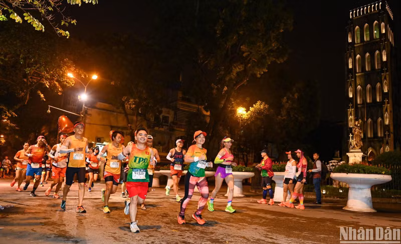 Pasan corriendo frente a la Catedral de San José de Hanói bajo las luces brillantes en la ciudad milenaria en la noche.