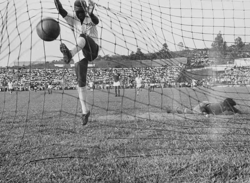 A nivel de clubes, Pelé solo jugó para dos equipos, el Santos y el New York Cosmos, con los que conquistó 27 trofeos. Esta imagen captura el momento en que Pelé salta a la red después de marcar un gol del Santos en un partido contra el equipo Guaraní de Paraguay en 1958. Pelé fichó por el Santos en 1956 y se convirtió en el "arma" que encumbró al equipo nacional e internacionalmente. (Fotografía: Pictorial Parade/Archive Photos/ Getty Images)