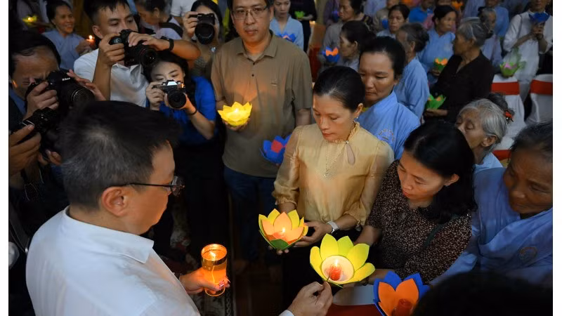 Le Quoc Minh, miembro del Comité Central del Partido Comunista de Vietnam y subjefe de su Comisión de Comunicación y Educación, presidente-editor del periódico Nhan Dan y titular de la Asociación nacional de Periodistas, pasa luminarias a otros participantes en la ceremonia.