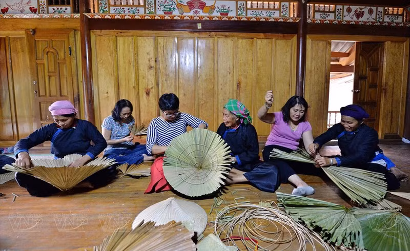 Turistas experimentan el tejido del sombrero cónico en la aldea de Lien.