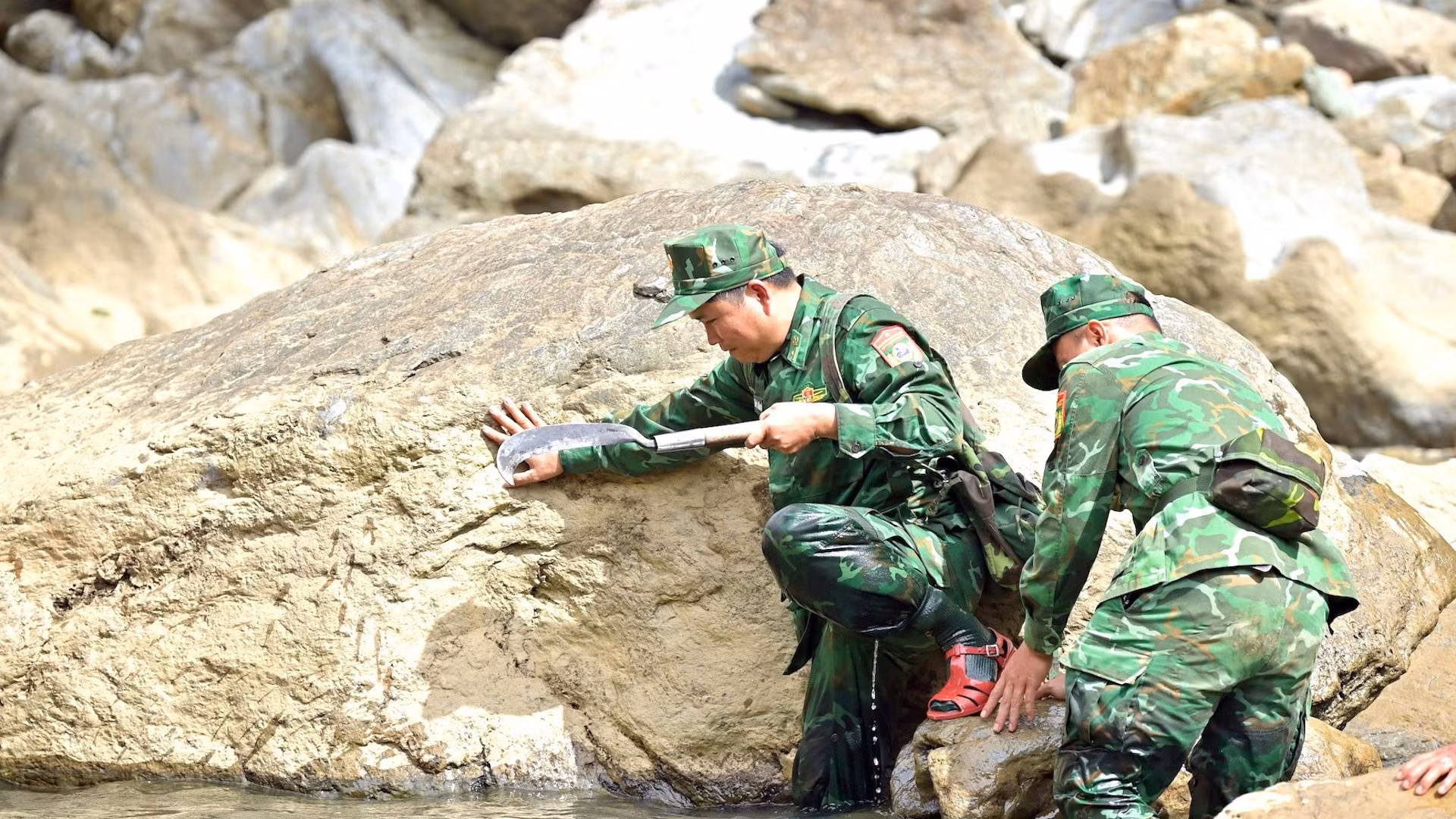 Dos soldados se apoyan mutuamente para atravesar un paso rocoso.