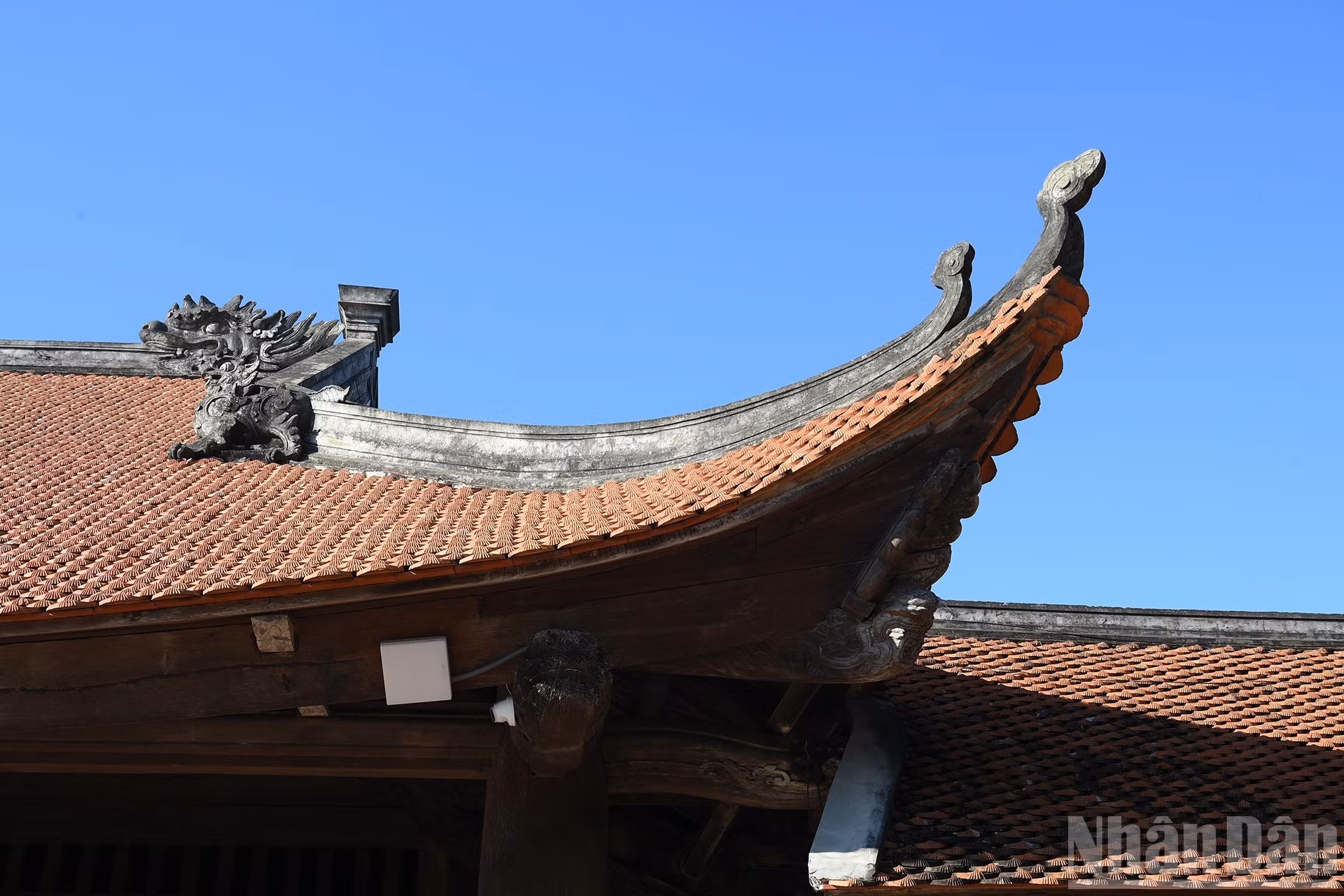 El campanario sobresale por su estructura de madera ensamblada mediante espigas tradicionales, sin utilizar clavos, y sostiene doce techos superpuestos con otros tantos aleros curvos que se recortan con elegancia sobre el cielo azul.