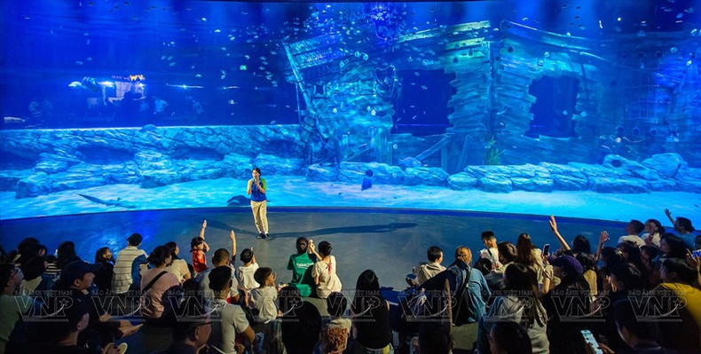 Turistas y niños escuchan una introducción sobre el Acuario Lotte World Hanói en la principal zona de tanques acrílicos curvos de mayor tamaño del Sudeste Asiático.