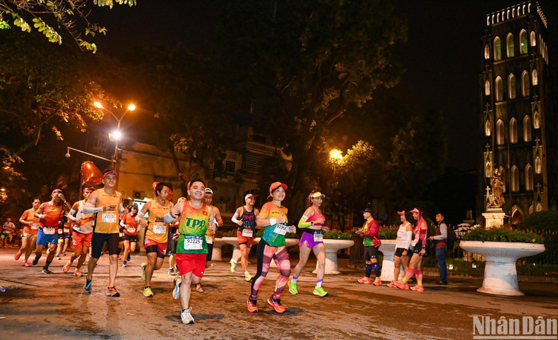 Pasan corriendo frente a la Catedral de San José de Hanói bajo las luces brillantes en la ciudad milenaria en la noche. Pasan corriendo frente a la Catedral de San José de Hanói bajo las luces brillantes en la ciudad milenaria en la noche.