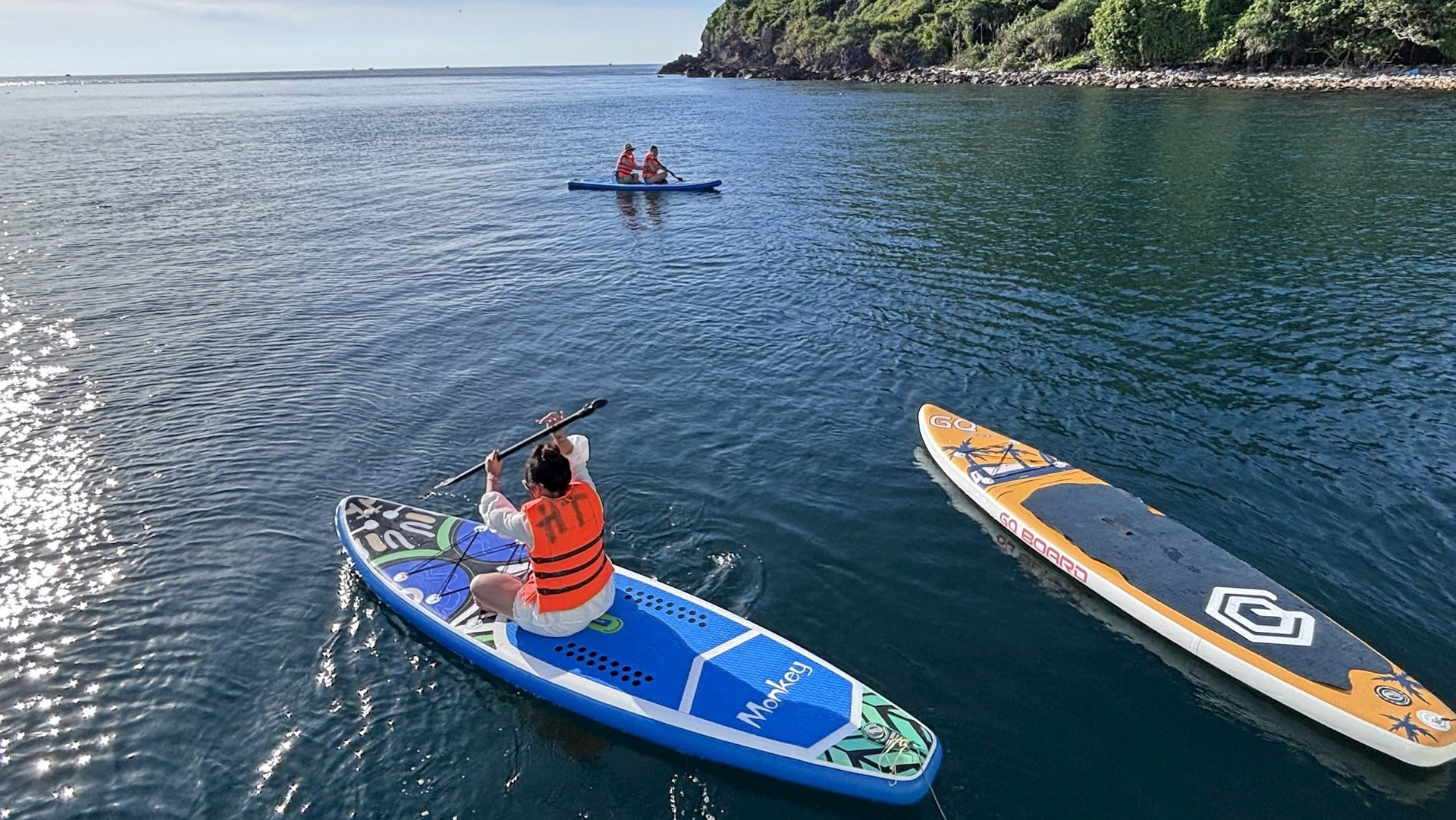 En otra playa tranquila, los visitantes pueden dejarse llevar sobre tablas de paddle surf que flotan suavemente en la superficie del agua. En otra playa tranquila, los visitantes pueden dejarse llevar sobre tablas de paddle surf que flotan suavemente en la superficie del agua.
