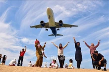 Turistas posan para una fotografía en la playa Mai Khao de Phuket mientras un avión aterriza en el aeropuerto internacional de Phuket (Foto: AFP/VNA)