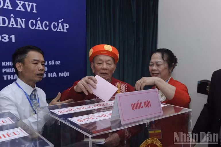 Un anciano ataviado con la túnica tradicional “ao dai” entra en la sala de votación con la ayuda de funcionarios. La escena, tomada en la circunscripción electoral 2 en el barrio de Nghia Do, en Hanói, emociona a quienes están alrededor.