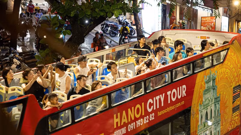 Numerosos turistas nacionales y extranjeros disfrutan contemplando la panorámica de Hanói de noche desde el espacio abierto del segundo piso de los autobuses turísticos. (Foto: VNA)