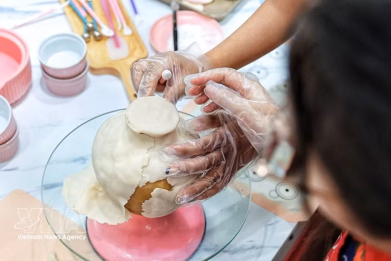 La artesana alisa y ajusta cuidadosamente cada parte de la masa que recubre el pastel de luna para dar forma al jarrón antes de decorarlo y combinarlo con las ramas florales de To he. (Foto: VNA)