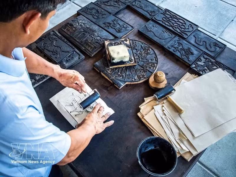 A partir de las planchas de madera talladas, el artesano utiliza tinta negra elaborada con ceniza de paja y hojas de plata para imprimir de forma uniforme el diseño sobre la superficie de la obra. (Foto: VNA)