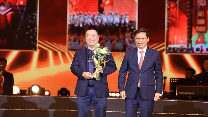 Tran Thanh Lam (derecha), miembro del Comité Central del Partido Comunista de Vietnam y subjefe de su Comisión de Propaganda y Movilización de Masas, entrega al redactor subjefe de Nhan Dan Que Dinh Nguyen la estatuilla honorífica dirigida al programa “La Patria en el corazón”. (Foto: Nhan Dan)