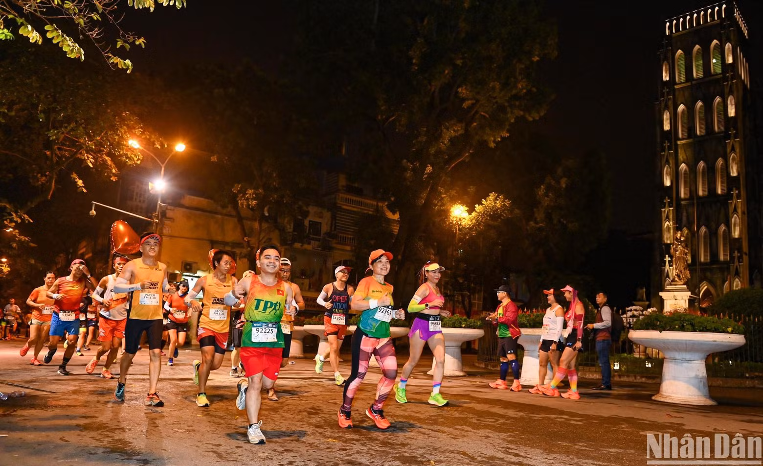 Pasan corriendo frente a la Catedral de San José de Hanói bajo las luces brillantes en la ciudad milenaria en la noche. Pasan corriendo frente a la Catedral de San José de Hanói bajo las luces brillantes en la ciudad milenaria en la noche.