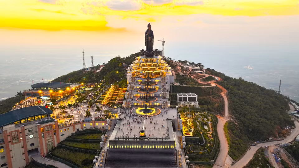 Vista panorámica del Área Turística Nacional de la montaña Ba Den al atardecer, destacando el conjunto de obras religiosas y el complejo arquitectónico iluminado con luces brillantes.