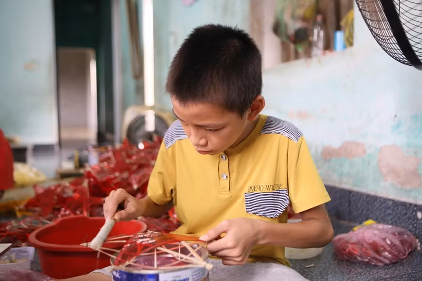Numerosos niños de la aldea de Bao Dap ayudan a sus padres en la producción de linternas con forma de estrellas durante las vacaciones escolares. (Fuente:VNA)