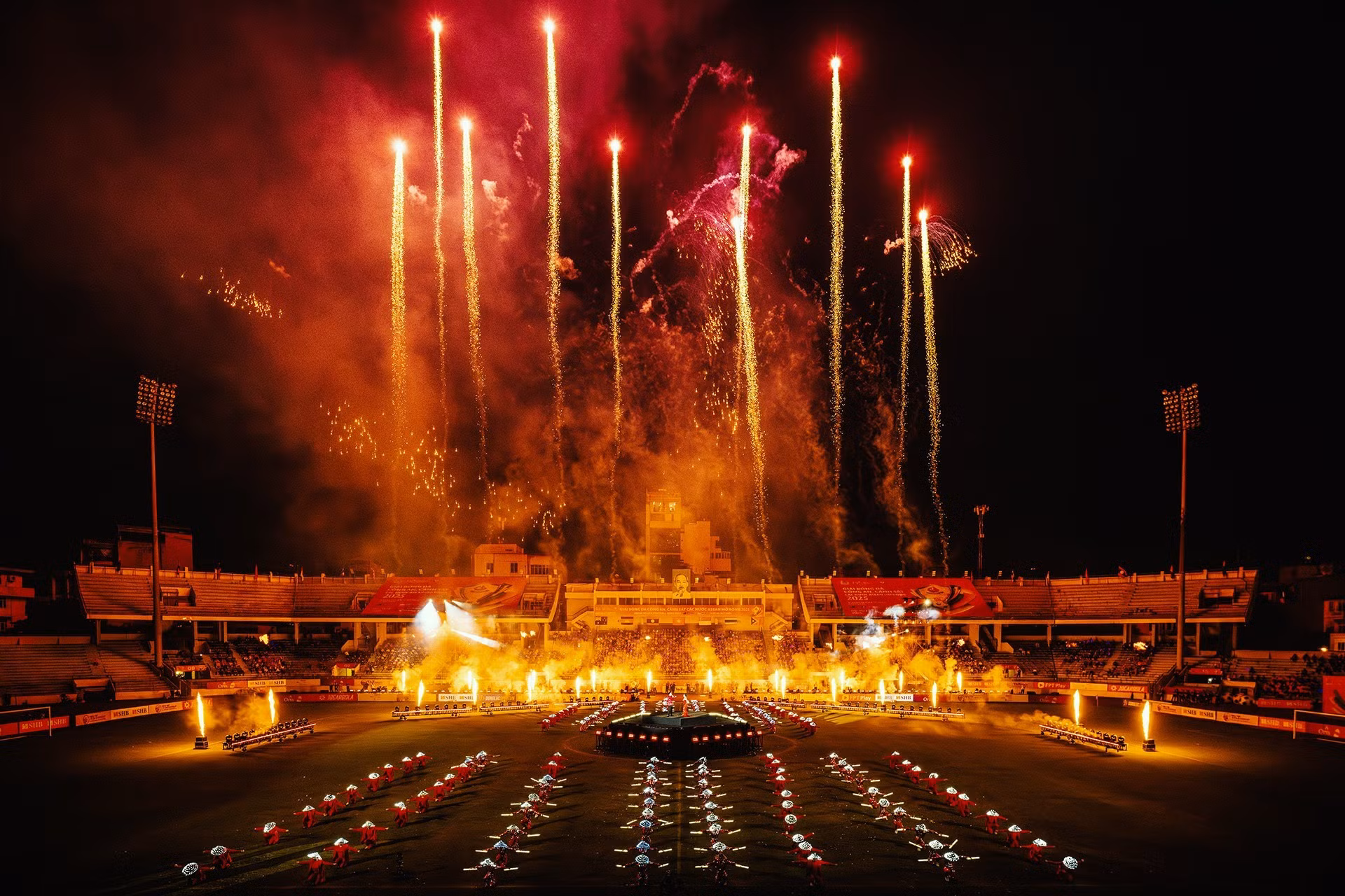 Las luces de los fuegos artificiales y los movimientos armoniosos de los artistas iluminan el estadio Hang Day con energía vibrante.