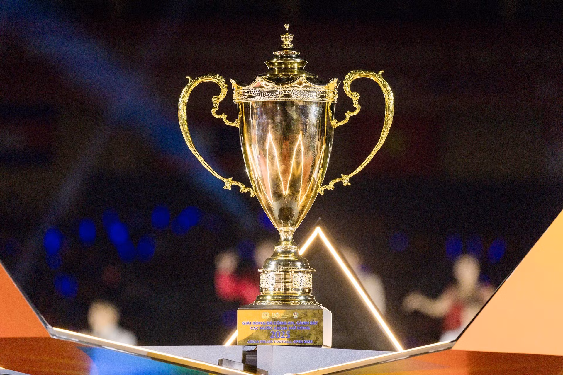 En medio de una brillante iluminación, el trofeo del campeonato aparece con solemnidad, símbolo del máximo honor al que aspiran los equipos competidores.