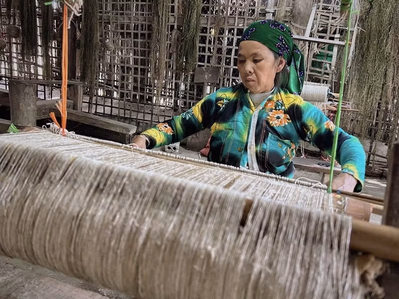 Una mujer Hmong en la aldea textil Lung Tam tejiendo telas a mano en telares de madera tradicionales.